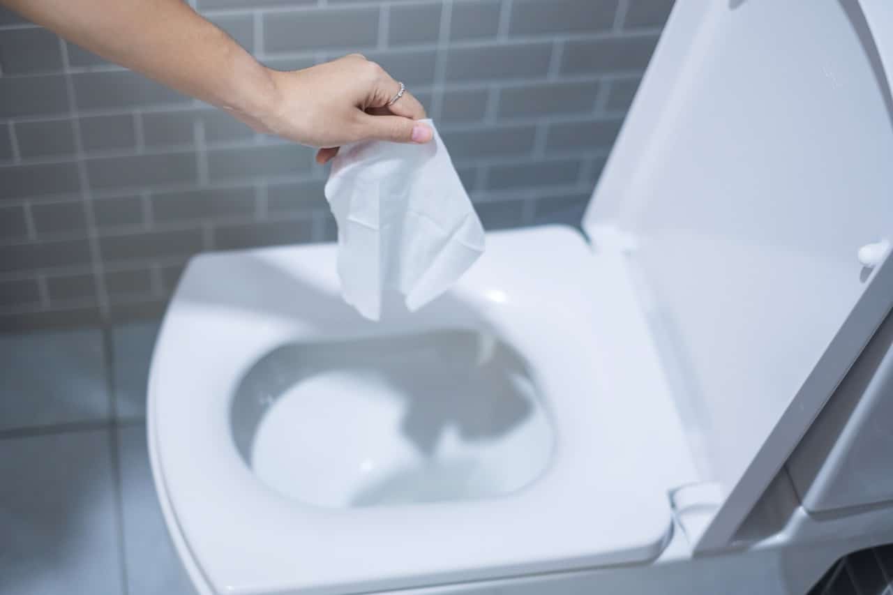 Woman hand disposing a wipe in a white toilet